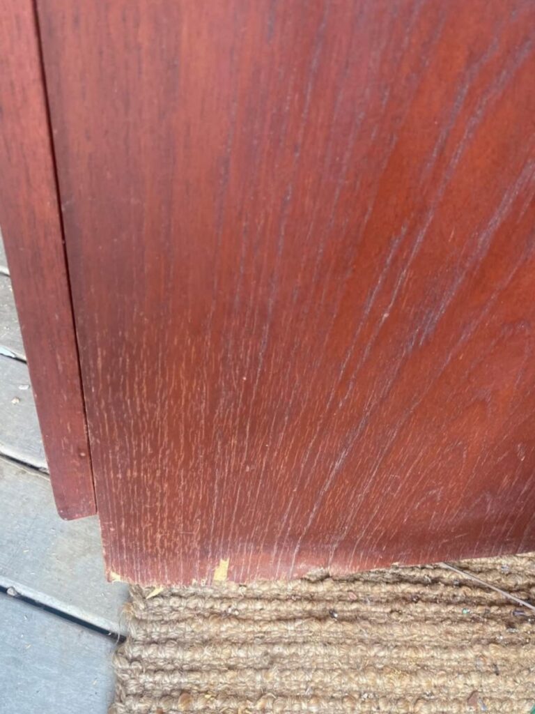 Side of the vintage teak veneer cabinet showing water damage, exposed chipboard and lifting veneer