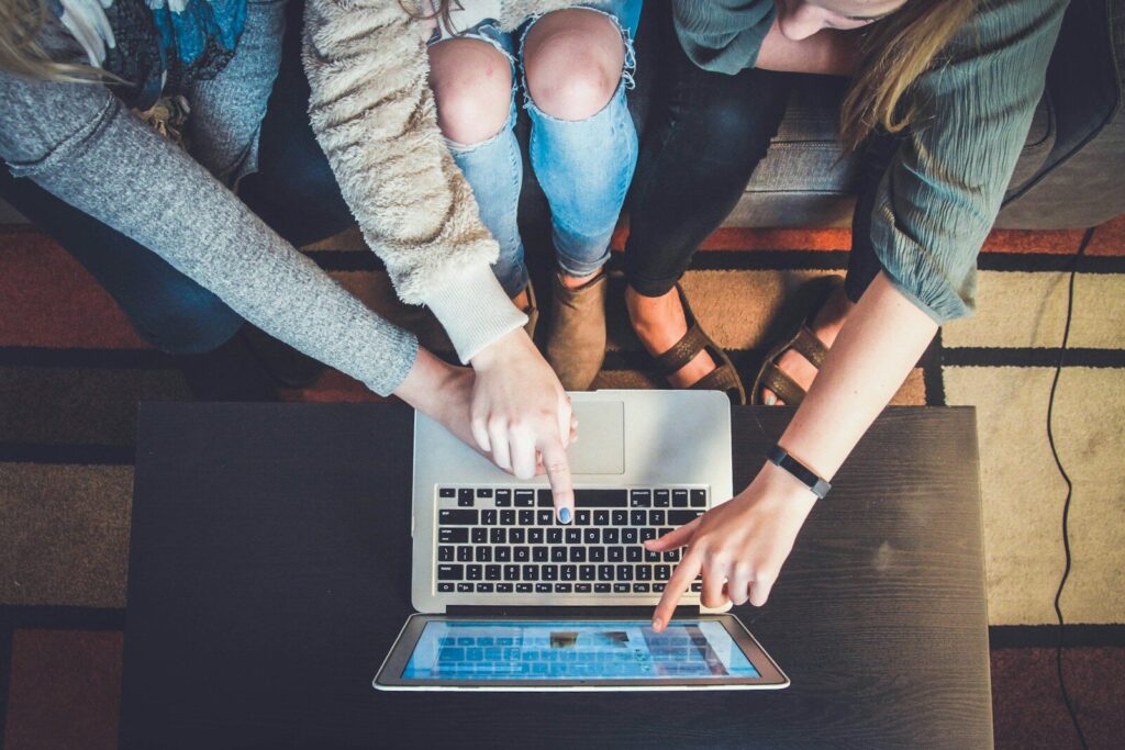 three people pointing to a silver laptop computer screen while online shopping