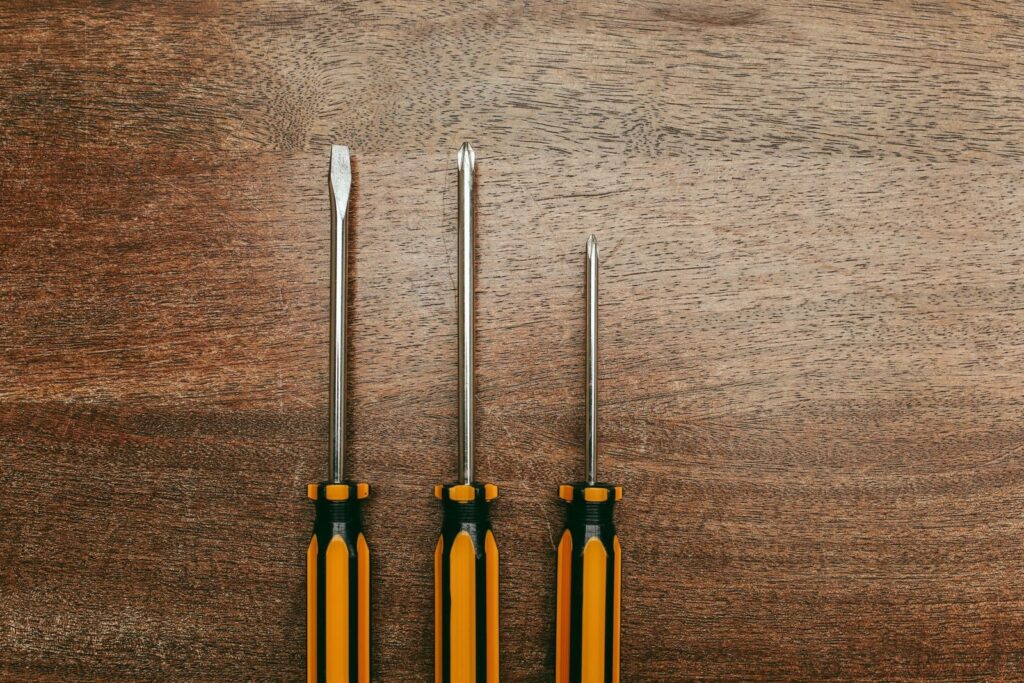 Top view of three screwdrivers laid out on a wooden surface, highlighting repair tools.