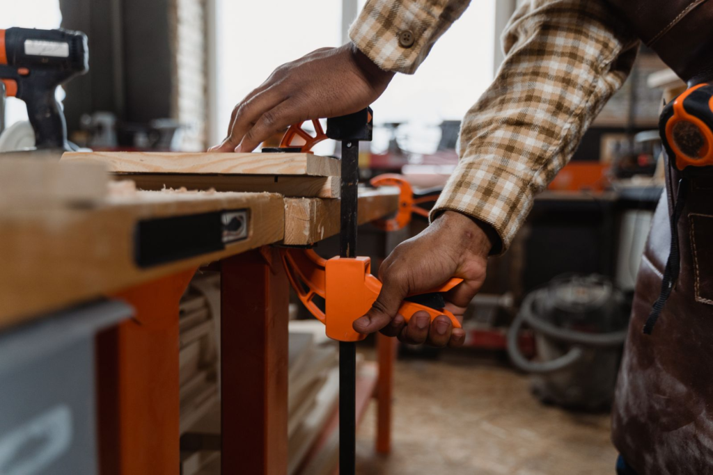 Hands clamping wood to a work bench using an adjustable clamp