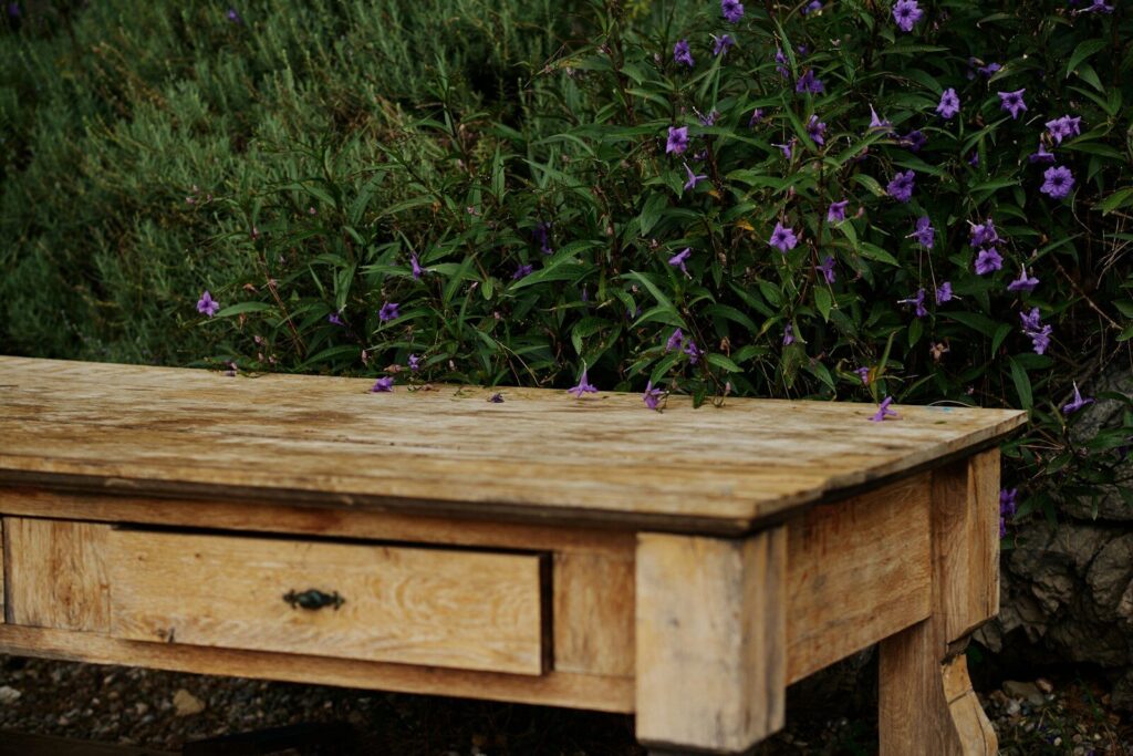 A weathered wooden solid timber table sits in a garden.