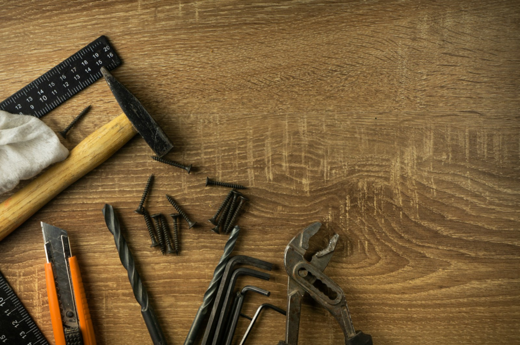 Tools including a hammer, square, drill bit, knife, Allan keys on a wooden surface