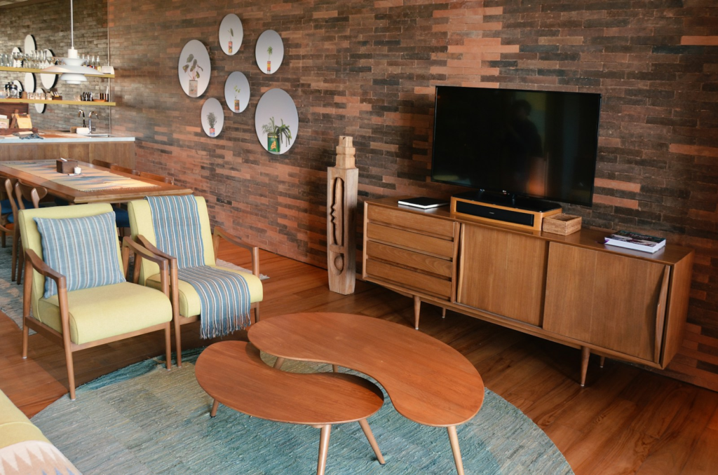 A mid-century modern living room with restored wooden furniture and a brick feature wall.