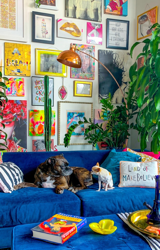 Eclectic colourful room with copper lamp, artwork, plants and dogs on a blue sofa 