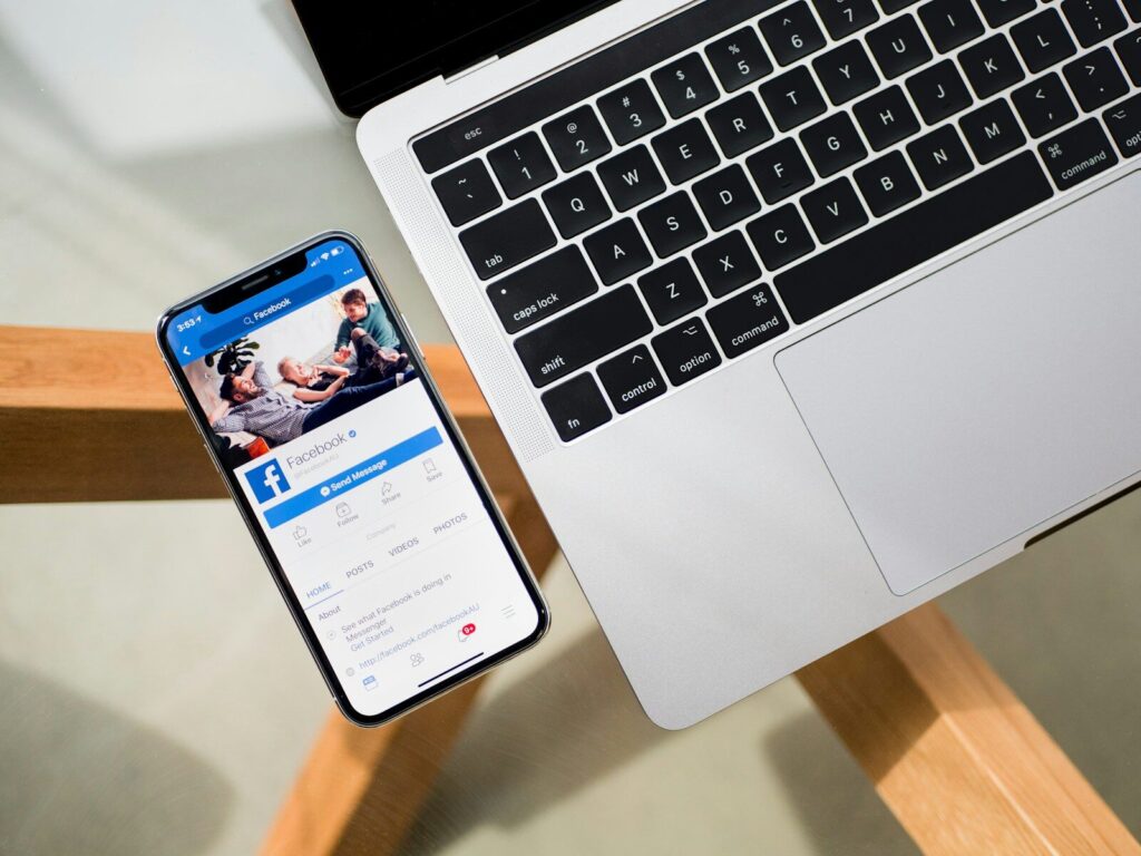 iPhone X beside MacBook showing Facebook on the phone screen