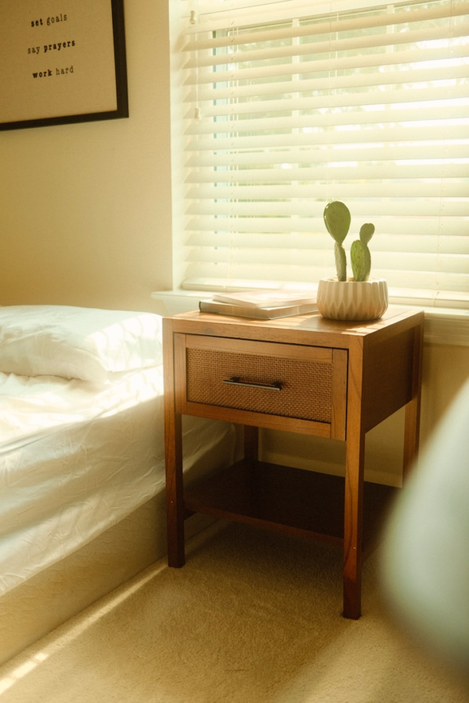 Bedside table next to a bed, styled with books and a cactus